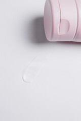 drop of white body cream smeared on a white background next to a pink closed tube