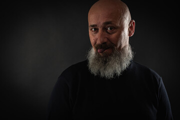 close up photo, portrait of a serious, thoughtful, bearded man on a dark background confident and dramatic looking straight. Concept of male portrait.  Low key 