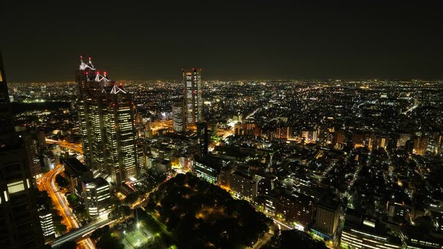 Large Asian city lights at night. Lively car lights motion on large street. Scenic Tokyo cityscape, aerial time lapse shot. Residential quarters spread till horizon line, office towers on left