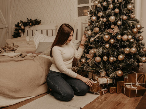 young woman sits in a white golf shirt near Christmas tree in bedroom