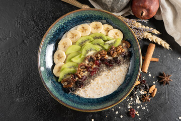 Oatmeal with chia seeds, banana, kiwi, walnuts and dried cranberries. A classic morning hot healthy breakfast of cereal porridge with fruits, nuts and dried fruits.