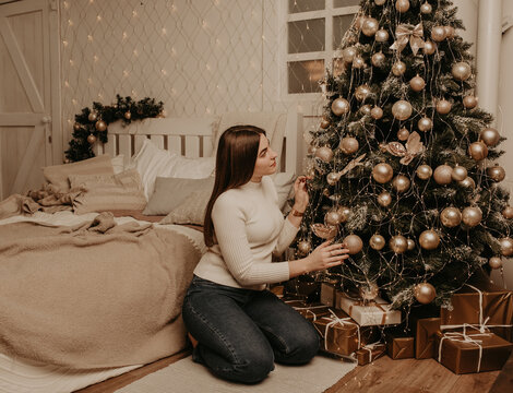 young woman sits in a white golf shirt near Christmas tree in bedroom