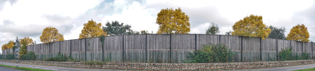 Fototapeta na wymiar Beautiful panorama of high fence in front of autumnal yellow trees along cycling path, Dublin, Ireland. Lens distortion is not corrected