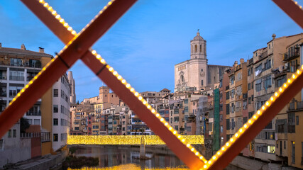 Girona's urban cityscape skyline at dusk with famous gothic cathedral landmark and river houses reflected on a quiet river from red iron bridge