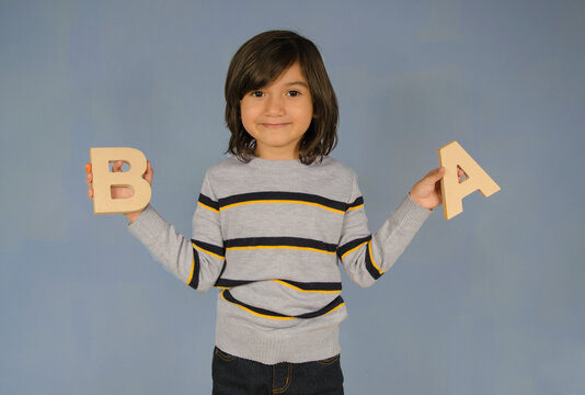 Latin kid&acute;s portrait smiling with blue background showing letters a and b