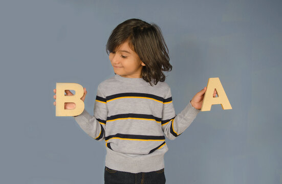 Latin kid&acute;s portrait smiling with blue background showing letters a and b and looking one of them