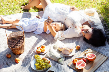 young pretty pregnant brunette woman having fun with her daughter on picnic on green grass in park, lifestyle people concept