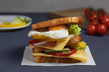 Homemade closed sandwich with cheese, bacon, egg, vegetables and lettuce