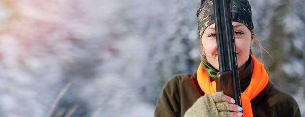 A young beautiful hunter woman on hunt in forest with rifle on the shoulder. Winter season. In the...