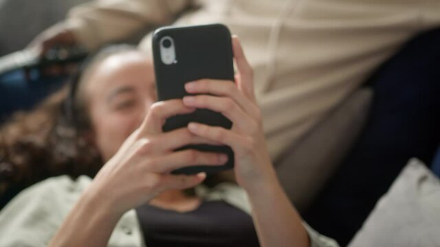 Close Up Of Relaxed Couple At Home On Sofa Watching TV And Checking Social Media On Mobile Phone