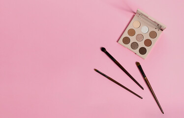  Daily eyeshadow palette in brown tones on a pink background top view with copy space. makeup brush, decorative cosmetics for the face. Flat lay female accessories. Nobody