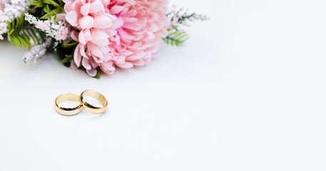 Pink flowers and two golden wedding rings on white background.	