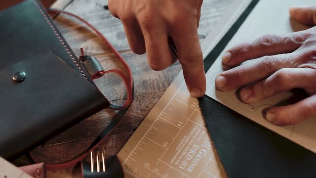 A craftsman cutting leather according to the pattern on wooden table in workshop