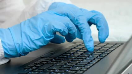 Closeup of fingers in medical gloves typing on laptop keyboard. People working from home and protecting from covid-19