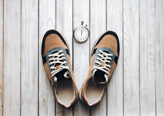 A new beige sport shoes (sneakers) from suede with stopwatch on white rustic wooden background. Training, jog and sport concept. Close up, top view.