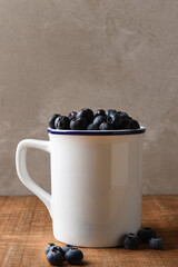 Obraz na płótnie Canvas Blueberry Still Life. A white mug filled with fresh picked Blueberries on a wood table. Vertical format with copy space.