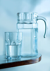 A pitcher and a glass filled with water, an overall light blue hue
