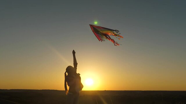 A happy girl runs with a kite in her hands across field in rays of the sunset. A healthy child dreams of freedom, flight. Kid plays outdoors in the park. Teen wants to be pilot