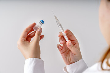 Close up on hand of unknown caucasian woman doctor holding syringe with needle and vaccine injection in front of white wall - covid-19 coronavirus vaccination concept healthcare and medicine