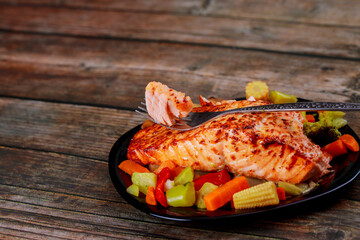 Tasty grilled salmon with asian stir-fry vegetables on black plate.