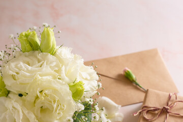Gift box and letter next to beautiful white flowers on pink marble background