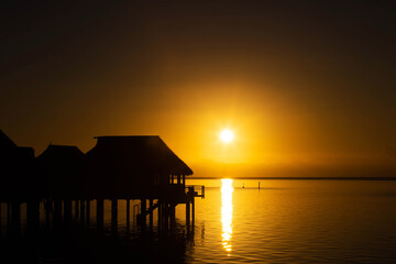 Fototapeta na wymiar Sun rises over tropical island ocean with vacation destination overwater bungalows