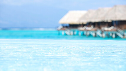 Beautiful clear turquoise water from an infinity pool into the tropical island ocean with overwater bungalows in the background
