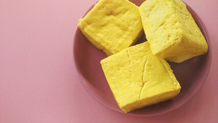 Yellow tofu made from soybeans, a traditional Indonesian food with a pink plate background