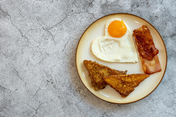 French toast, fried egg and bacon crispy in a ceramic plate on a cement floor. Top view.