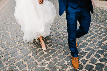 Obraz na płótnie Canvas The bride and groom holding on hands and walking on road in the nature. Outdoors. Down view at shoes.