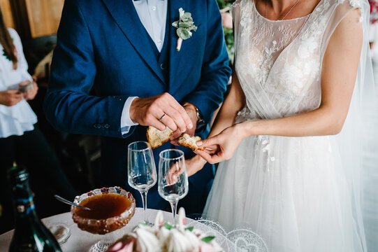 Close Up photo of bride and groom eating traditional loaf. Ukrainian and Russian wedding ceremony: bread with salt. Honey and glasses of champagne on an old rustic wooden table. Wedding traditions.