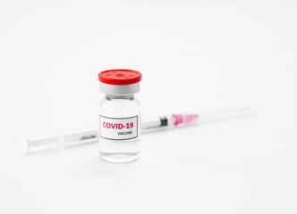 Clear vial with a red cap with the word covid-19 affixed to the side of the vial. Next to it is a...