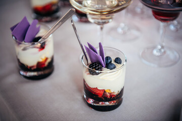 Delicious dessert of whipped cream and fresh berries in glass with spoon. Portioned sweet snacks in restaurant at festive banquet. Blackberries, blueberries, strawberries, berry topping, butter cream.
