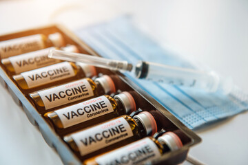 Coronavirus COVID-19 vaccine ampoules in a box, blurred background, close up. Vials with drug, label, syringe, medical mask, selective focus.