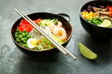 Bowls with tasty rice, shrimps and vegetables on dark background