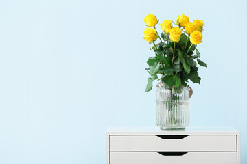 Vase with beautiful yellow roses on table against color background