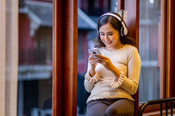 Obraz premium Beautiful woman with headphone sitting at the window sill while use mobile phone.