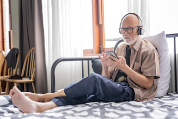 Old man with white beard take a rest in the room while listening music by headphone.