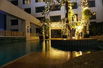 Night pool with beautiful lighting and wood. Romantic mood in hotels. The water reflects the light of the lights that are located on the tree in the middle of the pool and at the entrance. Thailand