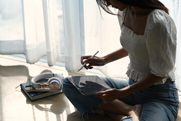 Young designer holding stylus pen drawing on digital tablet while sitting on wooden floor.