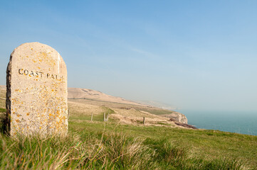 Old stone marker with faded carved Coast Path text and view of  sea and cliffs in background for...