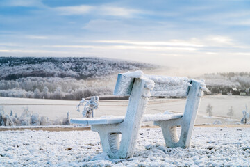 Winter mountains landscape and wooden iced bench in the morning
