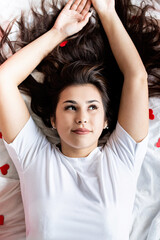 Fototapeta premium Young happy brunette woman laying in the bed with red heart shaped decorations
