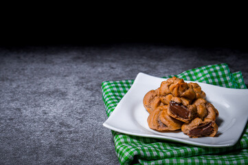 Put the chocolate filling cream in a white plate on top of a green patterned cloth set on a cement table.