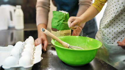 Little girl adding flour into large bowl beside grandmother
