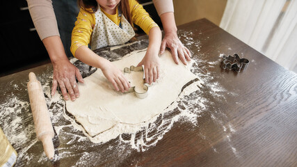 Top view of little girl cutting cookie from dough