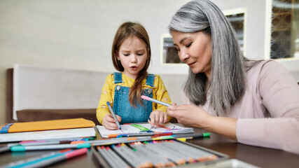 Cute little granddaughter drawing in album near grandmother