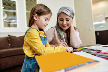 Grandmother sitting beside drawing little girl at home
