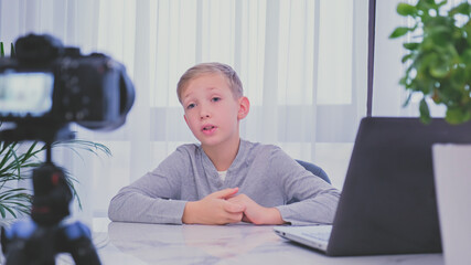Child blogger videotapes his vlog at home. Boy recording his video blog. White boy speaks in front...