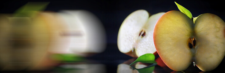Composition with apple slices on a black background. A slice of apple with back light on a black background with water drops. Juicy apple on a table.